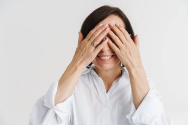 Avrupalı olgun bir kadın gülümserken beyaz duvarın üzerinden gözlerini kapatıyor.