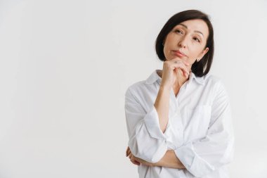 Avrupalı olgun kadın beyaz duvarın üzerinde izole bir şekilde kameraya poz verirken yana bakıyor