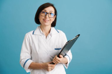 Avrupalı olgun doktor gülümserken mavi duvarın üzerinde izole bir panoyla poz veriyor