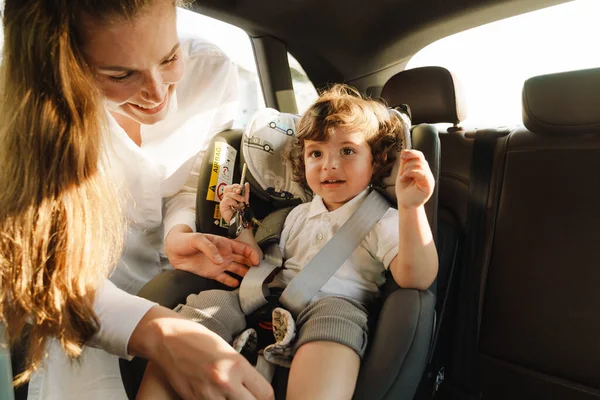 車の中で彼女の息子のシートベルトを身に着けている間 白い女性は微笑む — ストック写真