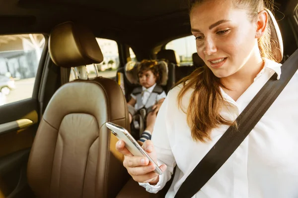 Young White Woman Using Cellphone While Going Car Her Son — Stock Photo, Image