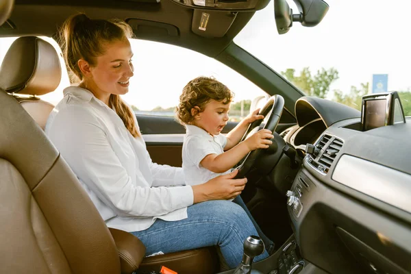 若いですホワイト女性笑顔と遊びます彼女の息子と一緒に座っている間車 — ストック写真