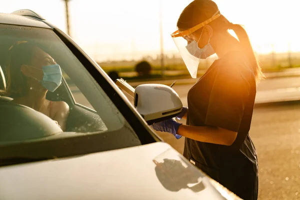 Schwarzer Gesundheitshelfer Mit Gesichtsmaske Notiert Notizen Während Autofahrer Spricht — Stockfoto