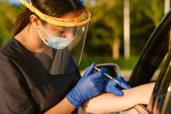 Black health worker in gloves making vaccine injection to white woman in car