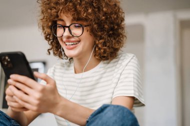 Mutfakta telefondaki gülümseyen genç kadın, kulaklıkla oturuyor.