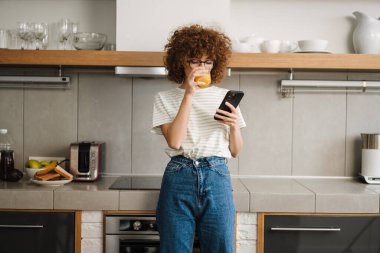 Mutfakta gülümseyen genç bir kadın, meyve suyu içiyor.