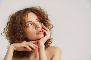 Yarı çıplak kızıl kadın beyaz arka planda yalnız poz veriyor ve yan bakıyor.