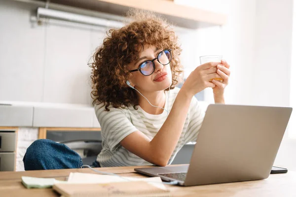 Mujer Pensamiento Europeo Usando Portátil Auriculares Mientras Bebe Jugo Cocina — Foto de Stock