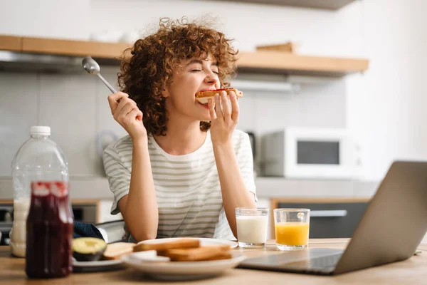 Mujer Joven Sonriente Usando Ordenador Portátil Mientras Desayuna Cocina Casera — Foto de Stock