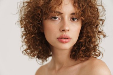 Yarı çıplak kızıl kadın beyaz arka planda yalnız poz verip kameraya bakıyor.