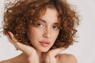 Yarı çıplak kızıl kadın beyaz arka planda yalnız poz verip kameraya bakıyor.