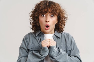 Kızıl saçlı genç kadın beyaz arka planda izole edilmiş kameraya şaşırdığını ifade ediyor.