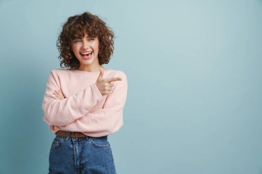 Genç kızıl mutlu kadın gülüyor ve mavi arka planda yalnız bir şekilde işaret ediyor.