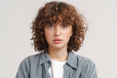 Genç kızıl hoşnutsuz kadın beyaz arka planda yalnız poz verip kameraya bakıyor.