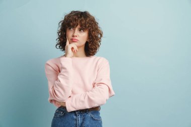 Genç, kızıl, ciddi bir kadın mavi arka planda izole edilmiş bir şekilde düşünüyor ve bakıyor.