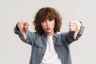 Kızıl saçlı genç kadın, beyaz arka planda izole bir şekilde baş parmağını aşağı gösteriyor.