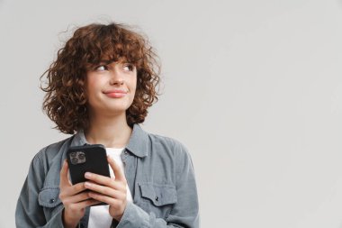 Beyaz arka planda izole edilmiş cep telefonu kullanırken gülümseyen kızıl saçlı genç kadın.