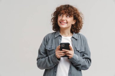 Beyaz arka planda izole edilmiş cep telefonu kullanırken gülümseyen kızıl saçlı genç kadın.