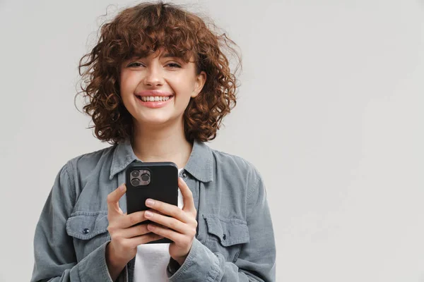 Wanita Muda Yang Gembira Tersenyum Sambil Menggunakan Ponsel Yang Terisolasi — Stok Foto