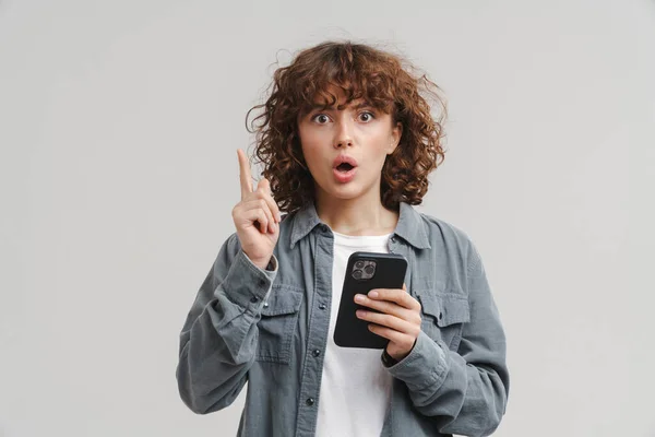 Ung Sjokkert Kvinne Med Pekefingeren Oppover Mens Hun Bruker Mobiltelefon – stockfoto