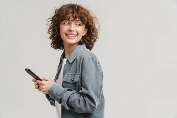 Wanita Muda Yang Gembira Tersenyum Sambil Menggunakan Ponsel Yang Terisolasi — Stok Foto