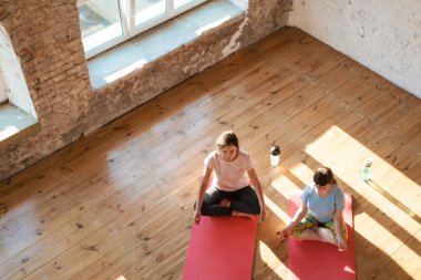 Down sendromlu genç bir kadın içeride koçla yoga dersi alıyor.