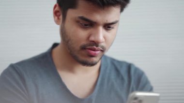 Tişört giyen neşeli Hintli adam evde telefona bakıyor.