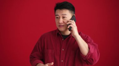 Kırmızı stüdyoda tişört giyen Asyalı adam telefonla konuşuyor.