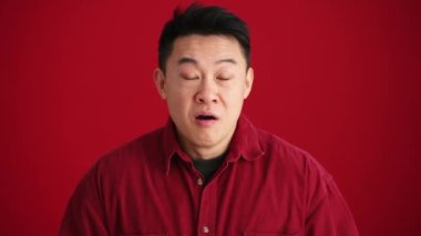 Kırmızı stüdyodaki kameraya şaşıran tişörtlü pozitif Asyalı adam.