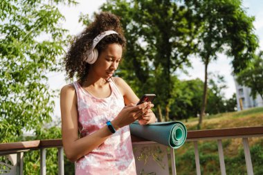 Siyah kadın merdivenlerde çalışırken cep telefonu ve kulaklık kullanıyor.