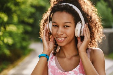 Yeşil Park 'ta egzersiz yaparken kulaklıkla müzik dinleyen genç siyahi bir kadın.