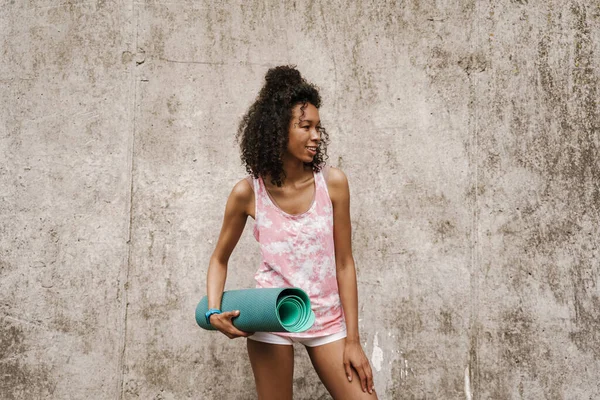 Mladá Černá Sportovkyně Usmívá Při Stání Fitness Podložkou Betonové Stěny — Stock fotografie