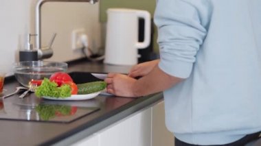 Sweatshirt giyen bir adam evde salata pişiriyor.