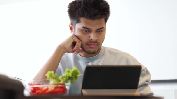 Hombre Indio Concentrado Usando Sudadera Comiendo Ensalada Escribiendo Por Tableta — Vídeo de stock