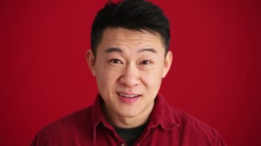 Kırmızı stüdyoda gömlek giyen neşeli Asyalı adam kameraya gözlerini açıyor.