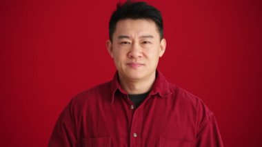 Kırmızı stüdyoda jest yapmayan, tişörtlü, konsantre Asyalı bir adam.