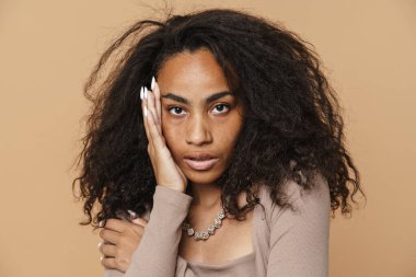 Kolyeli genç siyahi kadın bej arka planda izole edilmiş kameraya bakıyor.