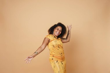 Bej arka planda izole bir şekilde dans ederken dövmeli genç bir kadın gülüyor.