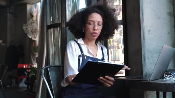 カフェでノートパソコンから何かを書いている集中女性 — ストック動画