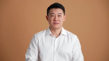 Beyaz gömlekli gülümseyen Asyalı adam turuncu stüdyodaki kameraya bakıyor.