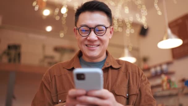 Rindo Asiático Jovem Vestindo Óculos Digitando Telefone Café — Vídeo de Stock