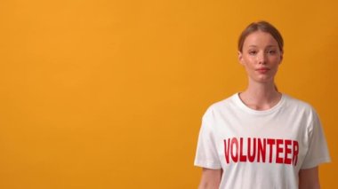 Pozitif kadın kameraya el sallıyor ve turuncu stüdyodaki boşluğu işaret ediyor.