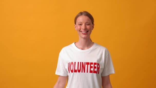 Glimlachende Vrouwelijke Vrijwilliger Wijzend Naar Haar Shirt Oranje Studio — Stockvideo