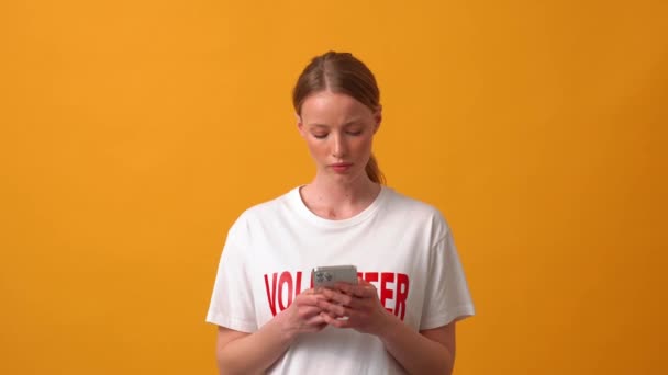 严肃的女性志愿者通过电话在橙色工作室打字 — 图库视频影像