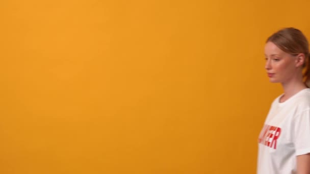 快乐的女性自愿地走着 指着她在橙色工作室里的T恤 — 图库视频影像