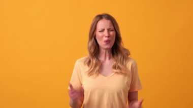 Sarı tişört giyen, turuncu stüdyodaki kameraya ne söyleyen sarışın kadın.