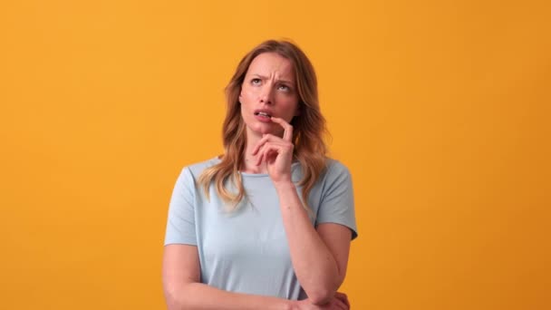 在橙色工作室里穿着蓝色T恤的多愁善感的金发女人在思考 — 图库视频影像