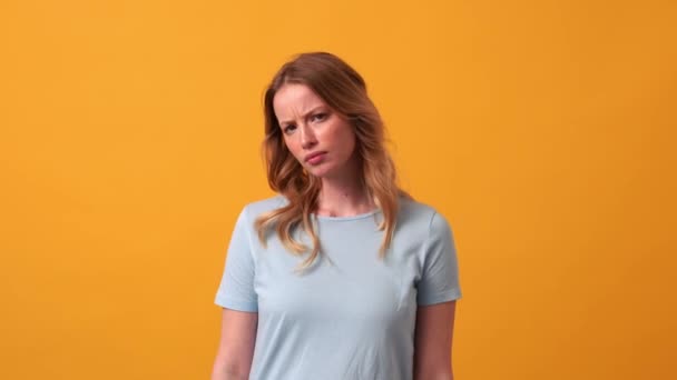 在橙色工作室里穿着蓝色T恤的不高兴的金发女人给出了否定的答案 — 图库视频影像