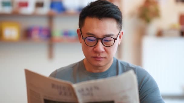Soustředěný Asijský Mladý Muž Nosí Brýle Čtení Novin Kavárně — Stock video