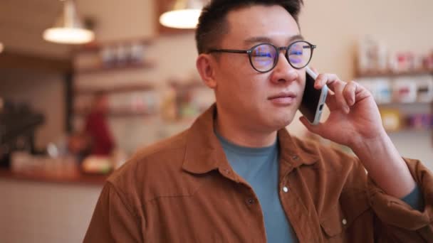 Veselý Asijský Mladý Muž Nosí Brýle Mluví Telefonu Kavárně — Stock video